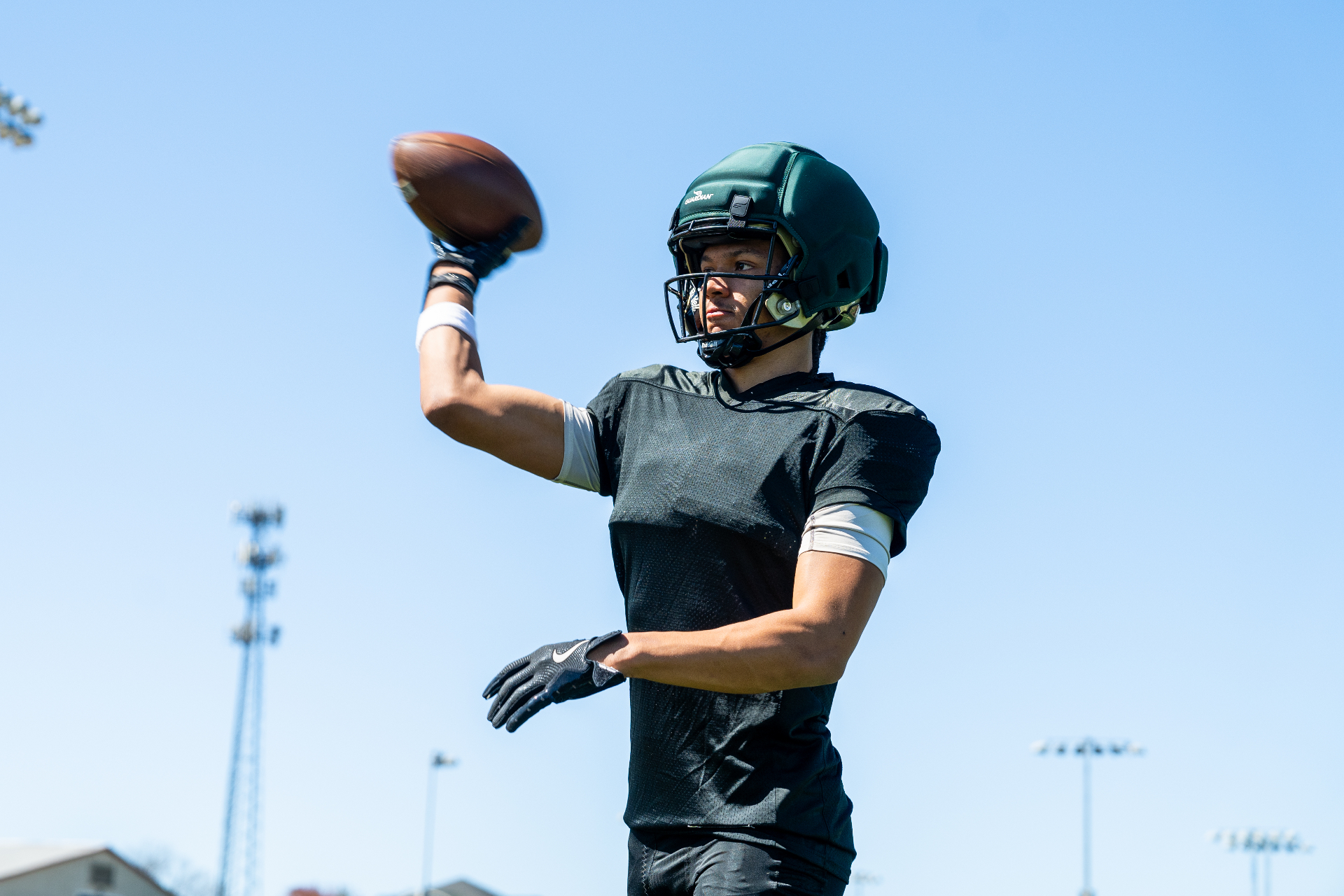 Quarterback in practice gear preparing to throw while wearing a green Guardian Cap