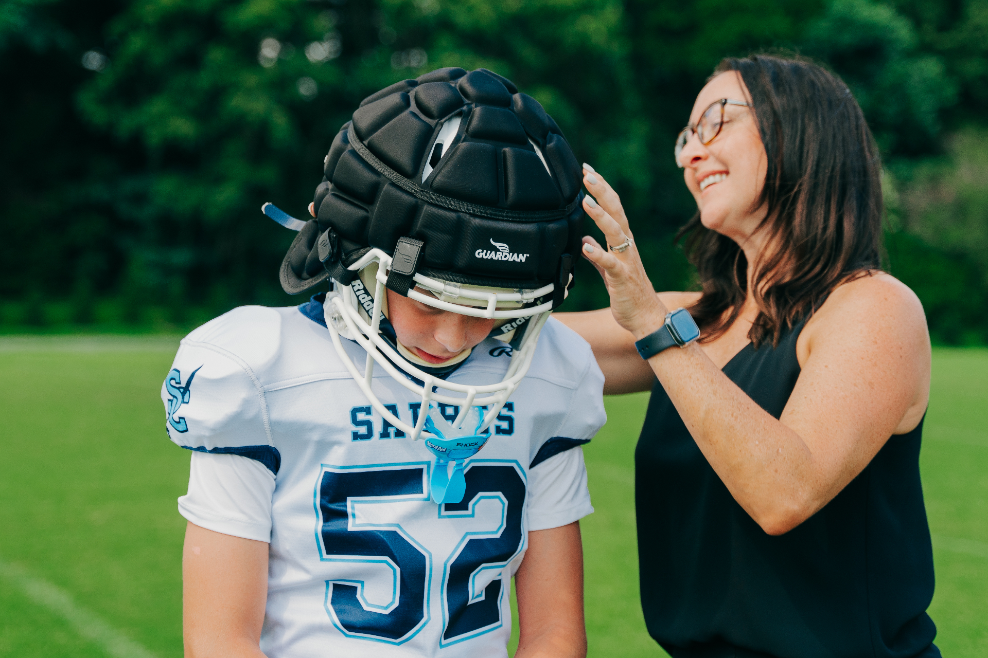 Adult helping fit a black Guardian Cap on a youth football player before practice